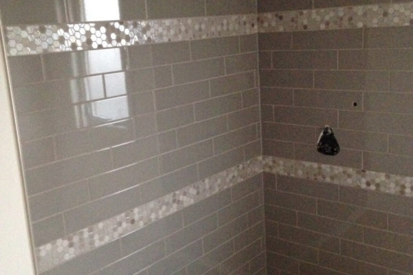 Shower stall with grey tile accented by vertical stripes of small hexagon tile.